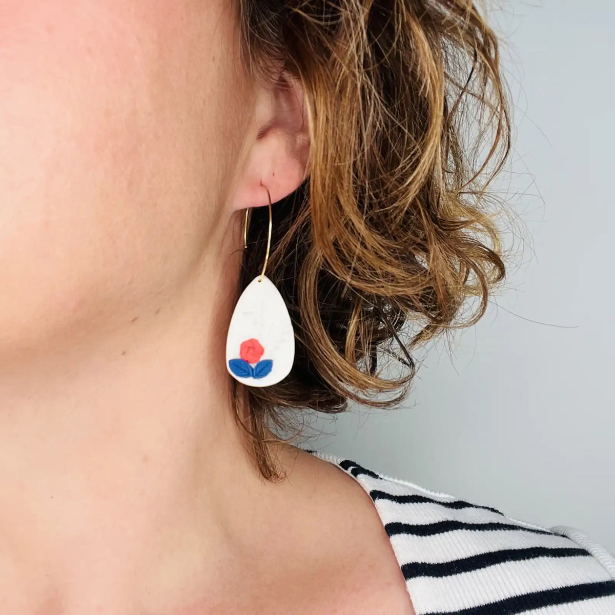 femme portant des boucles d'oreilles blanches décorées de fleurs rouges et bleues