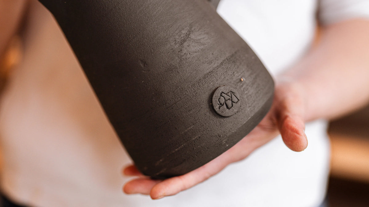 Mains tenant une carafe noire en grès, gros plan sur le logo Elephantom