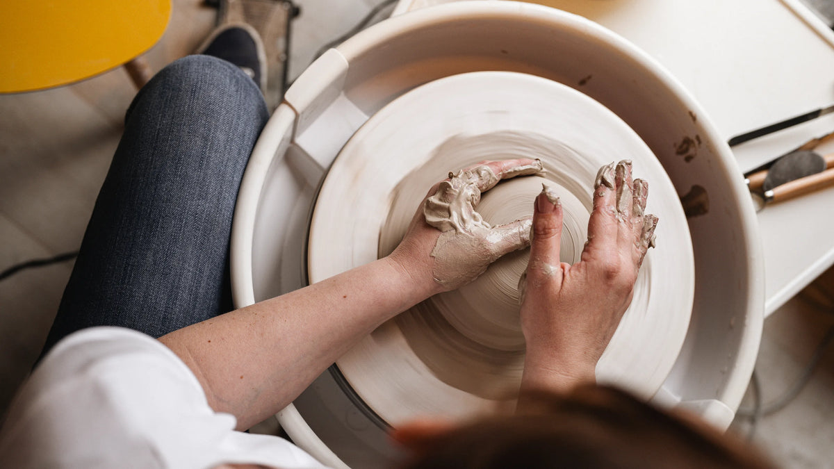 Mains d'une céramiste centrant une boule de grès sur le tour, atelier Elephantom