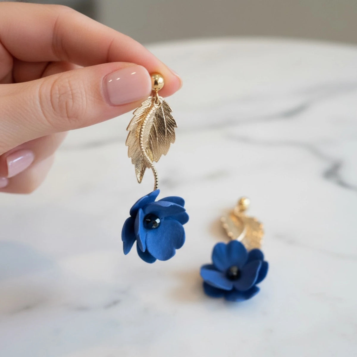 femme portant des boucles d'oreilles bleues en forme de fleur dans une main