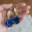femme portant des boucles d'oreilles bleues en forme de fleur  dans une main