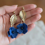 femme portant des boucles d'oreilles bleues en forme de fleur  dans une main