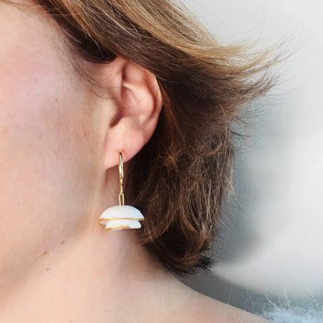 femme portant des boucles d'oreilles blanches et dorées au design floral 