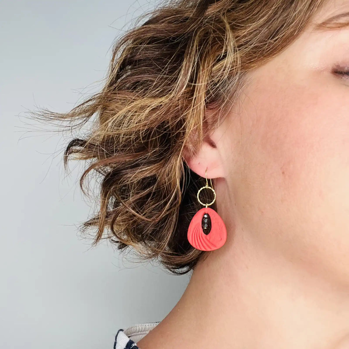 femme portant des boucles d'oreilles rouges décorées de de perles noires