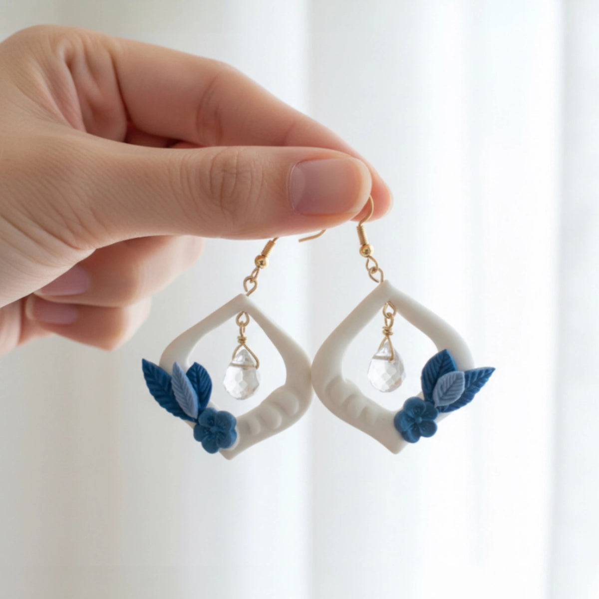 main tenant des boucles d'oreilles blanches et bleues au design floral 