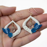 boucles d'oreilles blanches et bleues au design floral tenues dans une main