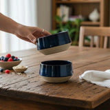 main déposant des bols empilables en grès pyrité beige et bleu  Elephantom