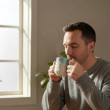 homme buvant son café dans son mug bleu turquoise avec motifs montagneux gravés